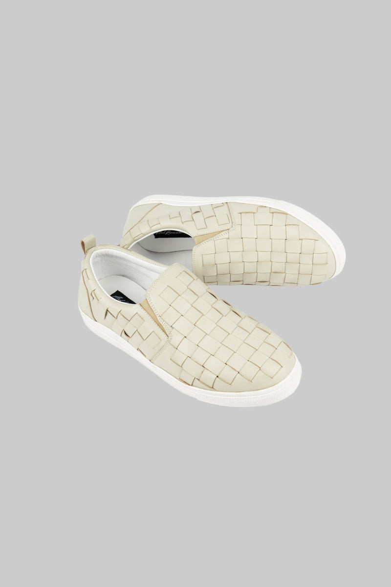 Pair of woven cream-colored slip-on shoes on a white background