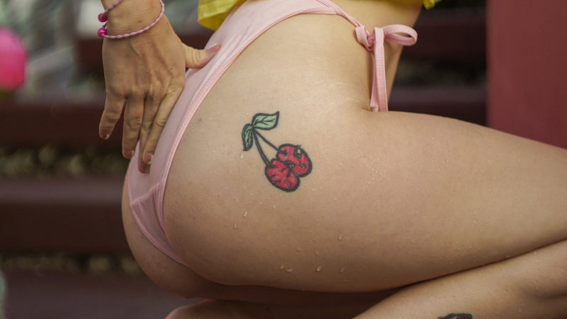 Person wearing a yellow top and pink underwear with tattoos on their legs.