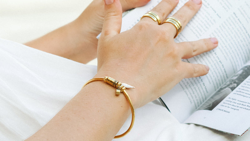 Close-up of hands with gold rings and bracelet on a white surface
